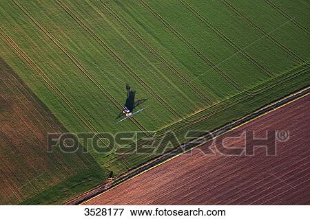 Stock Photo - France, Norhern France, Pas-de-Calais. Aerial view of an agricultural vehicle in a field. Fotosearch