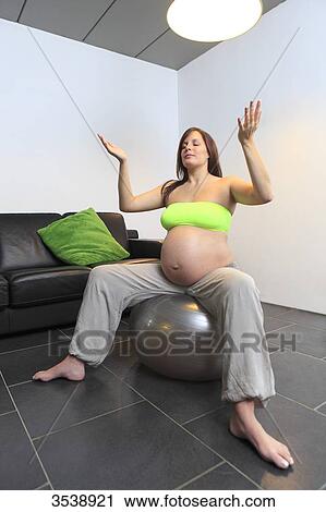 Stock Image - France, pregnant young woman doing yoga exercises on inflatable balloon. Fotosearch