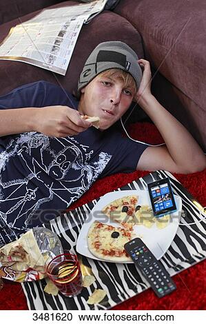 Stock Image - France teenager eating and watching TV. Fotosearch