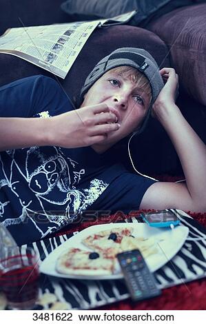 Stock Image - France teenager eating and watching TV. Fotosearch