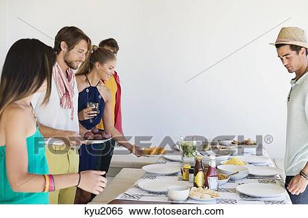 Friends arranging food on a dining table View Large Photo Image Stock Photography - Friends arranging food on a dining table. Fotosearch