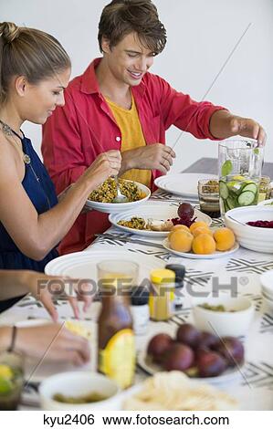 Friends sitting at a dining table having lunch View Large Photo Image Stock Photograph - Friends sitting at a dining table having lunch. Fotosearch