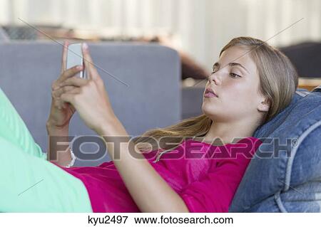 Stock Photo - Girl lying on a bean bag and using a mobile phone. Fotosearch