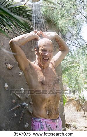 Stock Photography - Greece, Cyclades, smiling man taking a shower at the beach. Fotosearch