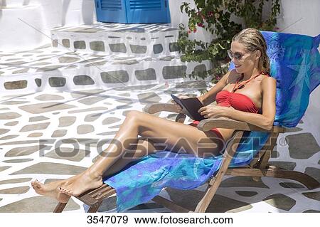 Greece, Cyclades, young woman reading on a deckchair View Large Photo Image Stock Photo - Greece, Cyclades, young woman reading on a deckchair. Fotosearch