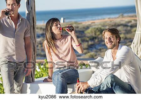Stock Photograph - Group of friends enjoying beer outdoors on vacation. Fotosearch