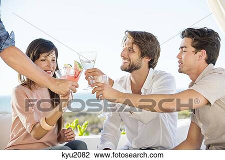 Stock Image - Group of friends toasting with drinks outdoors on vacation. Fotosearch