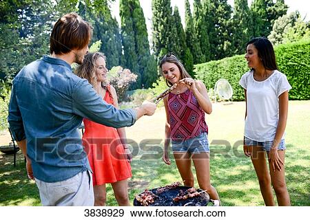 Stock Photo - Groupe of happy and cheerful young people having fun around barbecue grill during summer holiday party outdoor in the garden.. Fotosearch