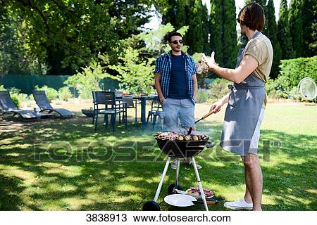 Handsome young man cooking meat in a barbecue party outdoor in the garden during summer holiday. View Large Photo Image Stock Image - Handsome young man cooking meat in a barbecue party outdoor in the garden during summer holiday.. Fotosearch