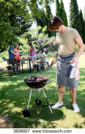 Handsome young man cooking meat in a barbecue party outdoor in the garden during summer holiday. View Large Photo Image Stock Photo - Handsome young man cooking meat in a barbecue party outdoor in the garden during summer holiday.. Fotosearch