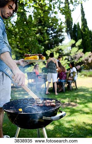Handsome young man cooking meat in a barbecue party outdoor in the garden during summer holiday. View Large Photo Image Stock Photography - Handsome young man cooking meat in a barbecue party outdoor in the garden during summer holiday.. Fotosearch
