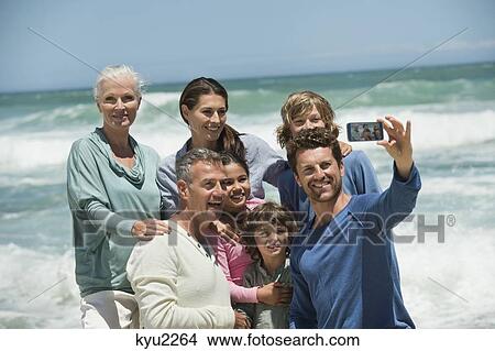 Picture - Happy multi-generation family taking a self portrait with a cell phone on the beach. Fotosearch