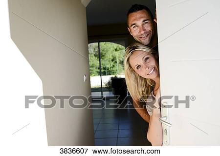 Stock Photo - Happy young couple welcoming friends at the front door of new house.. Fotosearch