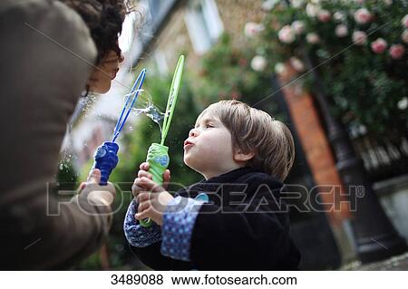 Stock Photo - Little boy and his mother blowing bubbles in the street. Fotosearch