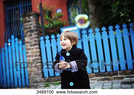 Stock Image - Little boy blowing bubbles in the street. Fotosearch