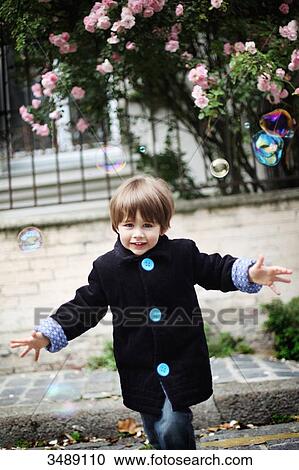 Stock Image - Little boy blowing bubbles in the street. Fotosearch