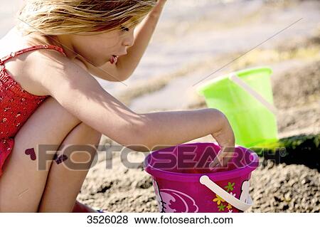 Litttle girl playing with a bucket on the beach View Large Photo Image Stock Photo - Litttle girl playing with a bucket on the beach. Fotosearch