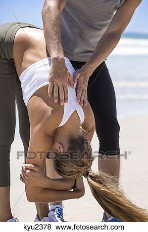 Stock Photo - Man helping woman stretch at beach. Fotosearch