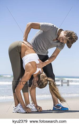 Stock Photo - Man helping woman stretch at beach. Fotosearch