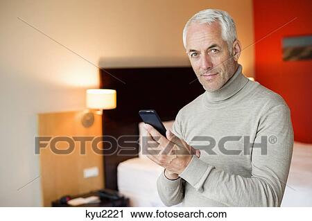 Stock Image - Man using a cell phone in a hotel room. Fotosearch
