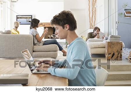 Stock Photo - Man using a laptop with his friends using electronic gadgets in background. Fotosearch