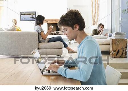 Man using a laptop with his friends using electronic gadgets in background View Large Photo Image Stock Photo - Man using a laptop with his friends using electronic gadgets in background. Fotosearch