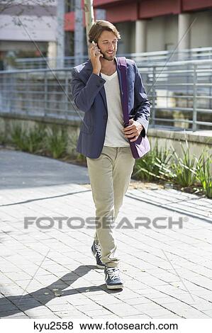 Stock Photo - Man walking on a street and talking on a mobile phone. Fotosearch