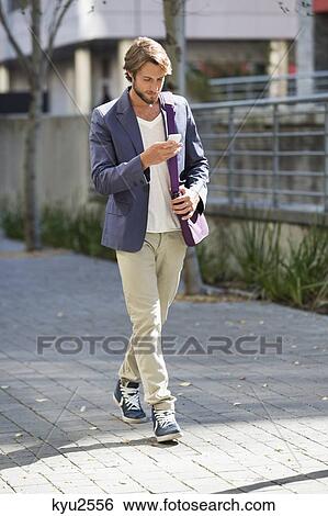 Man walking on a street reading text message View Large Photo Image Stock Photograph - Man walking on a street reading text message. Fotosearch