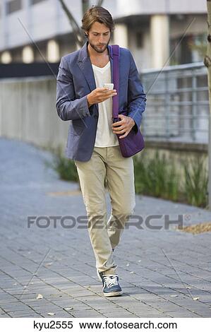 Stock Photography - Man walking on a street using a mobile phone. Fotosearch
