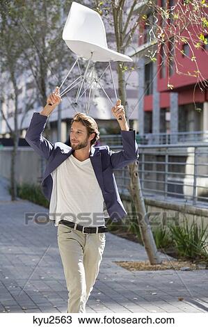 Man walking on a street with a chair View Large Photo Image Stock Image - Man walking on a street with a chair. Fotosearch