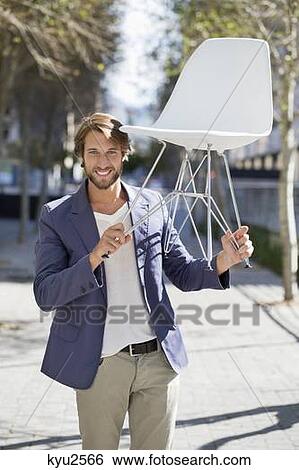 Stock Photograph - Man walking on a street with a chair. Fotosearch