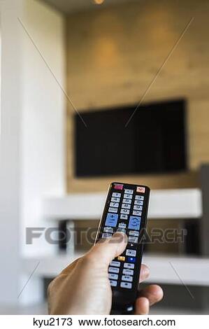 Stock Image - Person's hand operating a TV remote control. Fotosearch