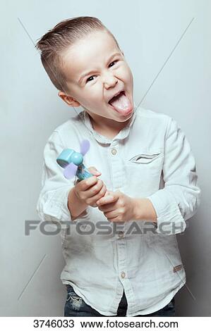 Stock Image - Portrait of a boy sticking his tongue out, a toy in hands. Fotosearch