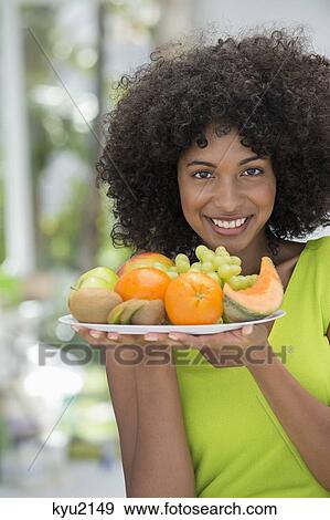Stock Photo - Portrait of a smiling woman holding a plate of fruits. Fotosearch