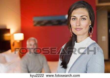 Stock Image - Portrait of a woman in a hotel room with her husband in the background. Fotosearch