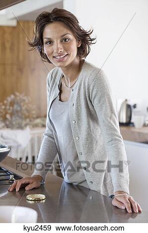 Portrait of a woman standing at kitchen counter and smiling View Large Photo Image Stock Photo - Portrait of a woman standing at kitchen counter and smiling. Fotosearch