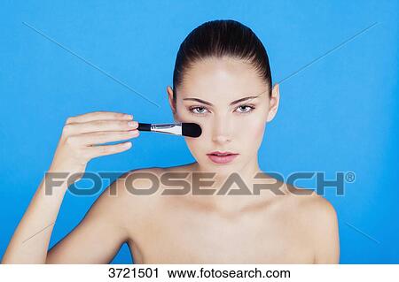 Stock Image - Portrait of a woman using make-up brush on face. Fotosearch