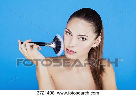 Stock Photo - Portrait of a woman using make-up brush on face. Fotosearch