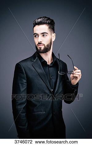 Portrait of a young businessman holding a pair of glasses, the look on the side View Large Photo Image Stock Image - Portrait of a young businessman holding a pair of glasses, the look on the side. Fotosearch