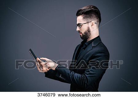 Stock Photo - Portrait of a young businessman upset, holding a touch pad in his hands. Fotosearch