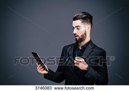 Portrait of a young shocked businessman holding a touch pad in his hands View Large Photo Image Stock Image - Portrait of a young shocked businessman holding a touch pad in his hands. Fotosearch