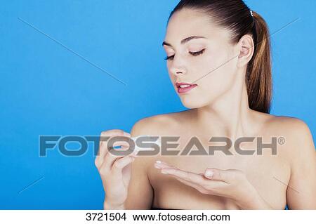 Picture - Portrait of a young woman applying lotion on her skin. Fotosearch