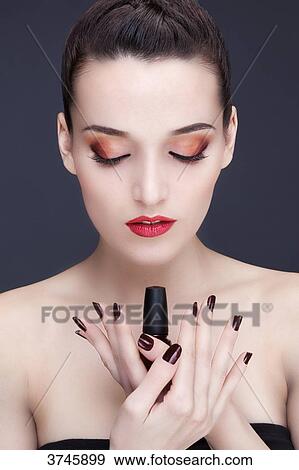 Stock Photo - Portrait of a young woman holding a nail polish bottle. Fotosearch