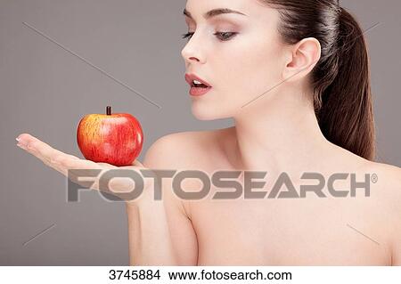 Picture - Portrait of a young woman looking and holding an apple in his hand. Fotosearch