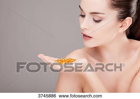 Stock Photograph - Portrait of a young woman looking for trace elements capsules in his hand. Fotosearch