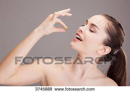 Portrait of a young woman preparing to take a capsule of trace elements View Large Photo Image Stock Photo - Portrait of a young woman preparing to take a capsule of trace elements. Fotosearch