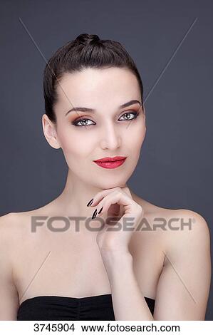 Portrait of a young woman smiling, hand under chin, looking toward the lens View Large Photo Image Picture - Portrait of a young woman smiling, hand under chin, looking toward the lens. Fotosearch