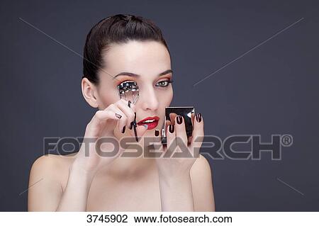 Stock Image - Portrait of a young woman using eyelash curler. Fotosearch