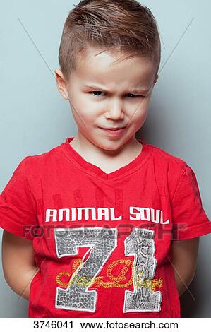 Stock Image - Portrait of an angry boy, arms behind his back, looking toward the lens. Fotosearch