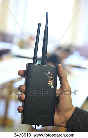 Stock Image - Room of examination for A Levels, closeup of a hand holding a mobile phones detector. Fotosearch